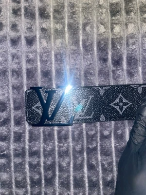 Loui  bälte - Snyggt svart bälte från L med klassiskt monogrammönster och stor L -logga i metall som spänne. Bältet har en exklusiv känsla och passar perfekt till jeans eller kostymbyxor. Materialet är skinn med tryckt mönster.