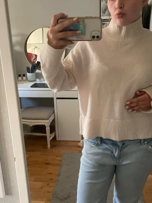 Beige stickad polotröja - Säljer en beige stickad polotröja med bred ribb vid hals, ärmslut och nederkant. Tröjan har en avslappnad passform och är gjord i mjukt material som känns skönt mot huden. Perfekt att matcha med jeans för en enkel och snygg look.