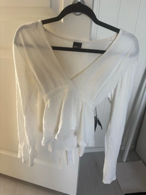 Vit omlottblus från Gina Tricot - Säljer en vit omlottblus från Gina Tricot med långärmad design och knytband i midjan. Använd fåtal gånger så fortfarande väldigt bra skick!