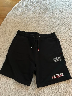 Svarta shorts från Hoodrich - Svarta shorts från Hoodrich med snörning i midjan, två sidofickor och tryckt logga samt patch-detalj på ena benet. Sköna och avslappnade, perfekta för sommaren. Materialet känns mjukt och är bomull eller polyester. Bara att höra av sig för fler bilder eller frågor . Tänk inte på att det står storlek L. De passar både S och M den är skum i storleken.