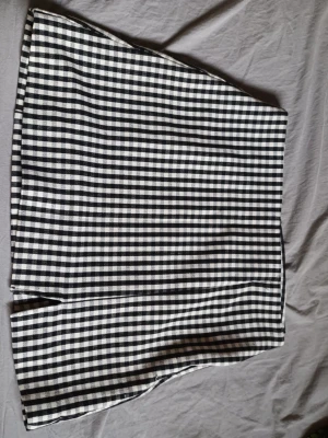 Svartvit rutig kortkjol med slits - Trendig svartvit rutig kortkjol med liten slits framtill. Kjolen har en rak passform och är tillverkad i ett mjukt tyg som känns bekvämt. Kjolen har en dragkedja på sidan där man stänger. Perfekt att styla med en enkel topp eller stickad tröja. Säljs då den inte används!!💕 storlek är M men skulle säga att den passar även på S💗