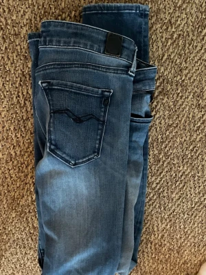 Blå jeans från 7 For All Mankind - Säljer ett par klassiska blå jeans från 7 For All Mankind med snygg tvätt och diskret broderad bakficka. Jeansen har normal passform och dragkedja i gylfen. Perfekta till din vardagsstil!