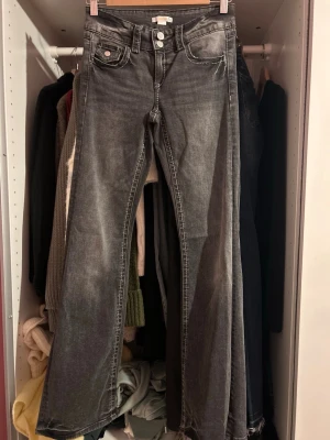 Grå bootcut jeans med slitningar - Snygga grå jeans med bootcut passform och slitningar. Klassiska femficksdetaljer och kontrastsömmar. Perfekta för dig som gillar en avslappnad och trendig look. Materialet är denim och färgen är tvättad grå.