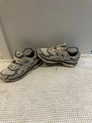 Gråa Asics sneakers mesh och mocka - Snygga sneakers från Asics i olika nyanser av grått. Ovandelen är i mesh och mocka för en sportig vibe och bra andningsförmåga. Klassisk snörning och låg profil gör dem perfekta till streetwear-looken. Sulan är robust och ger bra komfort hela dagen.