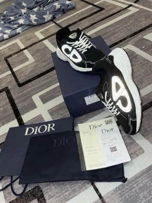 Svarta Dior B30 sneakers med reflex - Säljer ett par svarta Dior B30 sneakers med vit sula och stora reflekterande detaljer på sidorna. Skorna har mesh och läderpaneler, vita skosnören och tydlig Dior-logga. Snygg och modern design som sticker ut.