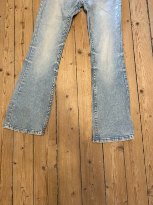 Ljusblå bootcut jeans - Säljer ett par ljusblå bootcut jeans med klassisk femficksdesign och lätt slitna detaljer framtill. Jeansen har utsvängda ben och är perfekta för en avslappnad och trendig look. Materialet är denim i bomull.