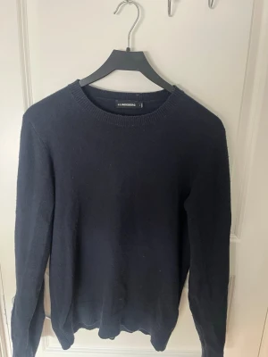 Mörkblå stickad tröja J.Lindeberg - Mörkblå stickad tröja från J.Lindeberg med rund halsringning och ribbade muddar vid ärmslut och nederkant. Klassisk och enkel design som passar till det mesta. Tillverkad i mjukt material för en skön känsla. Något nopprig men go ändå🙌
