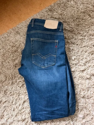 Blå jeans från Replay - Snygga blå jeans från Replay med klassisk femficksmodell och raka ben. Jeansen har ljus tvätt, kontrastsömmar och en vit Replay-lapp bak i midjan. Perfekta för en avslappnad och trendig stil. 32-32