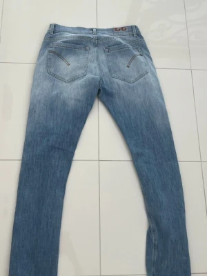 Dondup George Jeans - Säljer ett par ljusblå Dondup slim fit jeans med klassisk femficksdesign och snygga slitningar framtill. Jeansen har dragkedjegylf och raka ben. Perfekta för en avslappnad och trendig look. Helt oanvända. 