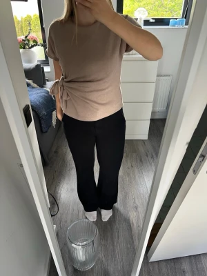 Beige topp med knyt från Zara - Snygg beige topp från Zara med korta ärmar och rund halsringning. Toppen har en unik knyt-detalj i sidan som ger en cool twist till outfiten. Använd endast ett fåtal gånger så väldigt bra skick!
