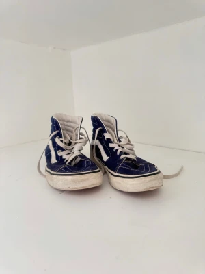 Blåa Vans Sk8-Hi sneakers - Ett par klassiska Vans Sk8-Hi sneakers i blå canvas med vita detaljer och vit sula. Skorna har den ikoniska sidoremsan och vita skosnören. Perfekta för en streetwear-look och funkar året runt. Köpte skorna för 750kr🥰