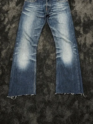 RARE Vintage Nudie Regular Ralf Bootcut #Archive - 🔥 Säljer ett par sjukt feta Nudie Jeans Regular Ralf🔥 Modellen släpptes ursprungligen redan 2001 och räknas som en av deras mest klassiska fits. Regular Ralf bytte senare namn till Regular Alf, vilket gör äldre par extra eftertraktade. Byxorna har helt galna naturliga fades som bara kommer från många års användning.  Storlek: W30 L34 men passar W30 L32, utgå från mått istället.   Mått:  Längd - 102 cm Midja - 41 cm Lår - 27 cm Benöppning - 22.5 cm Knä - 20 cm. Jeansen är avklippta några cm.