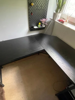 Amazon Svart L-format skrivbord i trä  - Säljer ett stilrent L-format skrivbord i svart trä med tydlig trästruktur. Perfekt för gaming, plugg eller hemmakontor. Bordet har gott om plats för dator, skärmar och tillbehör. Passar snyggt i hörn och ger en modern känsla till rummet.