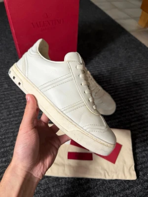 Valentino flycrew sneakers - Snygga vita sneakers från Valentino Garavani i äkta läder. Skorna har klassisk låg profil, vita snören och coola nitar på hälen som ger en unik touch. Perfekta för dig som gillar stilrena och exklusiva sneakers med lyxig känsla.