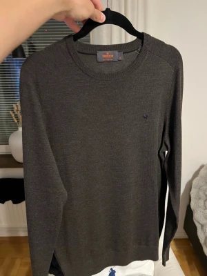 Mörkbrun stickad tröja från Morris - Snygg mörkbrun stickad tröja från Morris med rund halsringning och diskret broderad logga på bröstet. Tröjan har långa ärmar och är tillverkad i ett mjukt, tunt material som passar perfekt till lager-på-lager-stil.
