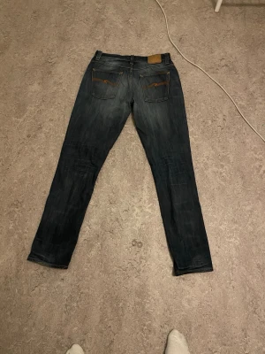 Mörkblå jeans från Nudie Jeans I grim Tim - Snygga mörkblå jeans från Nudie Jeans med klassisk femficksdesign och orangea sömmar. Jeansen har en rak passform och är tillverkade i denim med lätt slitning på framsidan för en cool look. Waist 33 Längd 34 