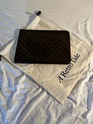 Louis Vuitton monogram datorfodral - Snyggt datorfodral från Louis Vuitton i klassiskt brunt monogrammönster. Fodralet är rektangulärt och tillverkat i canvas med LV-loggor över hela ytan. Perfekt för att skydda din laptop med stil.