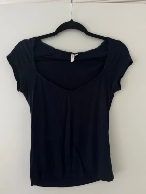 Mörkblå topp med v-ringning - En stilren mörkblå topp med v-ringad hals och korta ärmar. Toppen har en enkel och smickrande passform som passar till många olika stilar. Perfekt att matcha med jeans eller kjol för en snygg look.