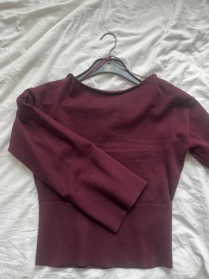 Vinröd v-ringad topp med lång ärm - Vinröd topp från Gina Young med v-ringning i ryggen och rund hals framtill. Långärmad modell i stretchigt, ribbat material som sitter snyggt på kroppen. Perfekt för dig som gillar stilrena och enkla plagg med en twist.