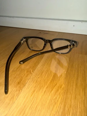Chrome hearts glasögon - Snygga glasögon med svart båge och rektangulär form. Bågarna har stilrena gulddetaljer vid gångjärnen som ger en lyxig känsla. Perfekt accessoar för att lyfta din look och addera en trendig touch.
