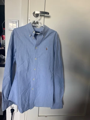 Blå skjorta från Ralph Lauren - Klassisk ljusblå skjorta från Ralph Lauren. Knappt använd utan defekter, tipsar för nån som är runt 165 