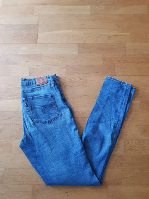 Levi's Sharping Skinny - Klassiska blå Levi's Sharping Skinny  jeans i rak modell med fem fickor och knappgylf. Jeansen har den ikoniska läderlappen bak i midjan och röd Levi's-tagg på bakfickan. Tillverkade i slitstark denim, perfekt för en avslappnad och tidlös stil.