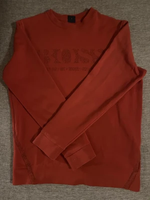 långärmad tröja från BOSS - Snygg långärmad tröja från BOSS med diskret logga framtill. Tröjan har rund halsringning och ribbade muddar vid ärmslut. Tillverkad i mjukt material som känns skönt mot huden. Perfekt för en stilren och avslappnad look. Små vita fläckar längst ut vid ärmen men inget som syns.