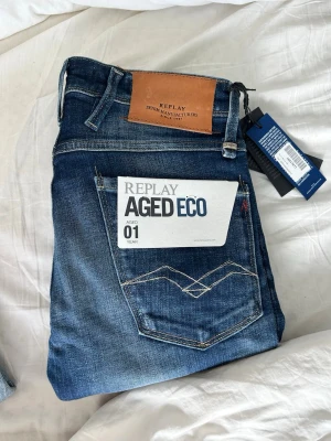 Replay Aged Eco jeans - Snygga blå jeans från Replay, modell Aged Eco. Jeansen har klassisk femficksdesign, läderpatch med logga bak och coola slitningar för en trendig look. Så sjukt snygg wash. Tillverkade i denim med miljövänlig behandling. Perfekta för dig som gillar stilrena och moderna jeans. Storlek 28. Helt nya. Ca 1 500 i nypris