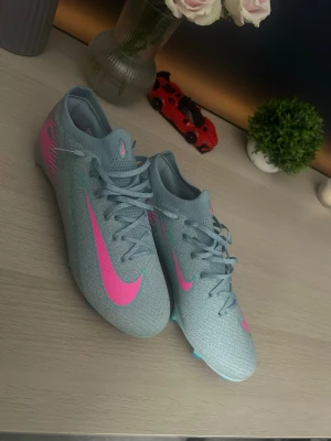 Fotbollsskor ”PRIS KAN DISKUTERAS” - Snygga Nike Mercurial fotbollsskor i ljusblå färg med neonrosa detaljer och logga. Skorna har en smal och aerodynamisk form med snörning och är tillverkade i syntetmaterial som ger bra grepp och känsla på planen.