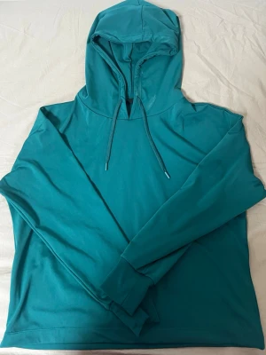 Turkos hoodie med dragsko - Snygg turkos hoodie med huva och dragsko. Hoodien har långa ärmar och en avslappnad passform, perfekt för en chill och stilren look. Tillverkad i mjukt material som känns skönt mot huden.