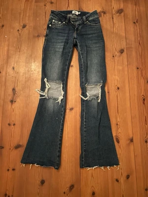 Mörkblå bootcut jeans med slitningar - Säljer ett par mörkblå bootcut jeans från Lager 157. Jeansen har klassisk femficksdesign och låg midja. Uppsprättad kant men annars inga defekter.