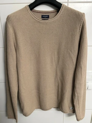 Beige stickad tröja Jack & Jones - Snygg beige stickad tröja från Jack & Jones med rund halsringning och diskret strukturmönster. Tröjan har långa ärmar och är tillverkad i ett mjukt material som passar perfekt för lager-på-lager-stil.