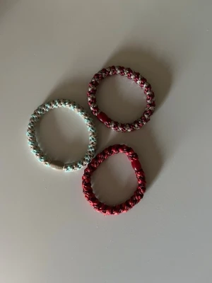 Färgglada spiralformade hårsnoddar - Tre spiralformade hårsnoddar i olika färger: en i rött, en i rött och silver samt en i turkos och vitt. Tillverkade i elastiskt material med glansig finish, perfekta för att sätta upp håret på ett snyggt och trendigt sätt.