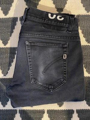 Svarta skinny jeans från Dondup - Säljer ett par svarta jeans från Dondup med klassisk femficksdesign och diskret D-logga på bakfickan. Jeansen har smal passform och är tillverkade i ett stretchigt material för extra komfort. Perfekta för en trendig och avslappnad look.