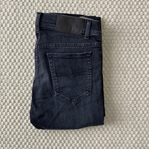 Svarta skinny jeans - Snygga svarta skinny jeans med klassisk femficksdesign och svarta detaljer vid linningen. Jeansen har en smal passform och är tillverkade i stretchigt denimtyg för en bekväm känsla. Perfekta för dig som gillar en stilren och modern look.