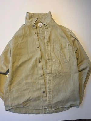 H&M Overshirt Skjortjacka Grön/Khaki  - Grön/khakifärgad overshirt från H&M i twill/bomullsmaterial. Bröstficka, knäppning fram, klassisk skjortkrage. Skönt tjockare tyg, funkar både som skjorta öppen över t-shirt eller knäppt som lätt jacka.  Skick: Mycket bra – knappt använd, inga fläckar eller skador.  Storlek: S  Öppen för bud/prisförslag 😊   Skickas snabbt 📦