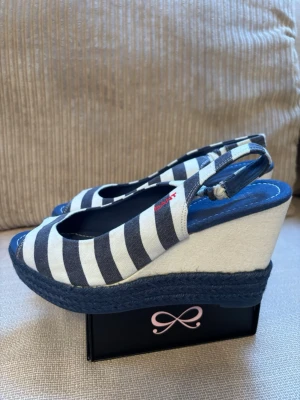 Randiga kilklackssandaler från Gant - Säljer ett par snygga sandaler från Gant med marinblå och vita ränder. De har öppen tå, kilklack i repimitation och justerbar rem bak. Ovandelen är i tyg och sulan är blå. Perfekta för en somrig look! Köparen betalar frakten. 