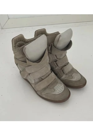 Isabell Marant skor  - Snygga beige sneakers med högt skaft och breda kardborreband. Skorna har en chunky design med mockadetaljer och perforerad tå. Tjock plös och vadderad kant ger extra komfort. Perfekta för dig som gillar streetstyle och vill sticka ut.