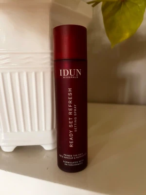 IDUN Minerals Ready Set Refresh mist - Face mist från IDUN Minerals i en mörkröd cylinderformad flaska. Ready Set Refresh är en setting spray som fräschar upp huden och fixerar makeup. Innehåller 3% niacinamid och är vegansk. Flaskan är tillverkad av återvunnen plast och rymmer 100 ml.
