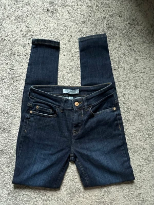 Mörkblå skinny jeans från JDY - Snygga mörkblå skinny jeans från JDY med klassisk femficksdesign och guldfärgade detaljer. Jeansen har smal passform och normal midja, perfekta till en avslappnad stil. Materialet är stretchigt denim som sitter bekvämt hela dagen.