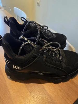 Chunky svarta sneakers från Buffalo - Chunky svarta sneakers från Buffalo med tjock sula och detaljer i både mesh och syntet. Skorna har svarta och vita snören samt logga på plösen och hälen. Perfekta för dig som gillar streetwear och vill ha en statement-look. Extremt bekväma skor och i mycket gott skick. Använda vid 2-3 tillfällen och välomhändertagna. 