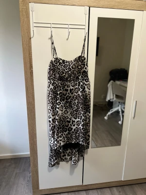 Leopardmönstrad klänning med smala band (pris kan diskuteras) - Säljer en snygg leopardmönstrad klänning med smala axelband och lätt draperad byst. Klänningen har en asymmetrisk nederkant som är längre bak och är tillverkad i ett mjukt, lätt material. Perfekt för dig som vill ha en lätt och skön klänning på dig i sommar eller andra årstider.