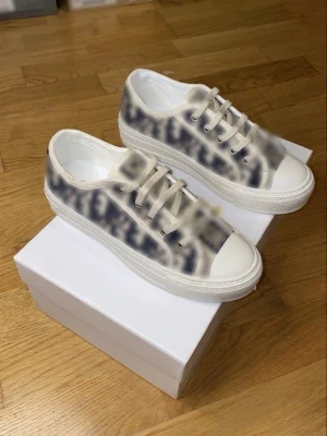 Beige och vita låga sneakers - Snygga låga sneakers i beige och vitt med mönstrad ovandel och vita snören. Skorna har en tjock vit sula och tåparti i gummi. Perfekta för dig som vill ha en trendig och stilren look. Passar till jeans eller kjol för en avslappnad vibe.