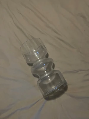 Snygg glas vas  - Säljer en genomskinlig vas med en snygg vågig design. Vasen har en bred botten, smal midja och rundad topp. Perfekt för dig som gillar annorlunda former och vill ha något fint att sätta blommor i. (Den är större än vad den ser ut, kan skicka en bild till de som vill där jag jämnför med något annat)