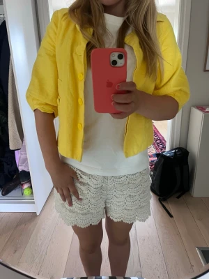 Gul kort jacka med knappar - Snygg gul jacka i kort modell med trekvartsärmar och stora knappar framtill. Jackan har klassisk krage och är tillverkad i ett lätt linneliknande material. Perfekt för att liva upp din outfit med en färgklick.