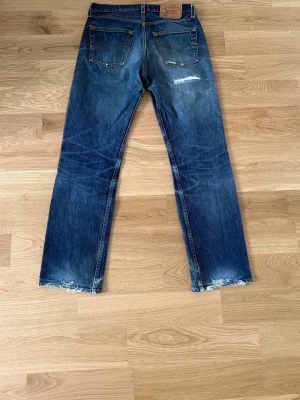 Levis 501XX Blå Jeans - Säljer ett par blå jeans med raka ben och tydliga slitningar vid knä och benslut. Jeansen har klassisk femficksdesign och en vintage tvätt som ger en cool, avslappnad look. 