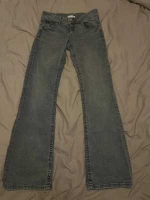 Grå bootcut jeans med låg midja - Säljer ett par grå bootcut jeans med låg midja. Jeansen har en lätt utsvängd passform nedtill och är tillverkade i denim. Perfekta för dig som gillar en avslappnad men ändå snygg stil.