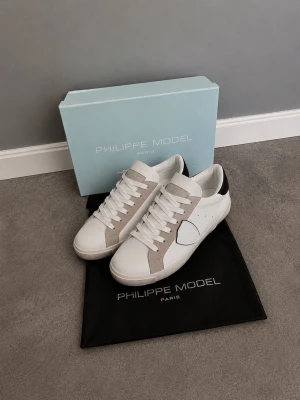 Vita Philippe Model Sneakers Low PRSXi skinn - Stilrena vita sneakers från Philippe Model i skinn med grå mockadetaljer och svart hälparti. Klassisk låg modell med vita snören och diskret logga på sidan. Perfekta för dig som gillar minimalistisk och trendig design. Dustbag medföljer.
