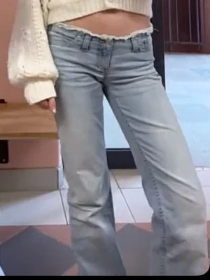 Ljusblå bootcut jeans med låg midja - Säljer ett par ljusblå  bootcut jeans med låg midja och slitna detaljer. Jeansen har klassisk femficksmodell och är tillverkade i denim med lätt stretch. Perfekta för dig som gillar retrovibbar och relaxed fit.