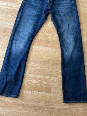 Replay jeans - Ett par Replay Waitom jeans i en mörkblå tvätt. Jeansen har en klassisk design med fem fickor och knappgylf. De har kontrasterande sömmar och en Replay-logotyp på myntfickan samt en läderlapp med Replay Blue Jeans-märkning baktill i midjan. Fruktansvärt snygga men var tyvärr lite för stora för mig. Kan fixa mått och bilder om det behövs.